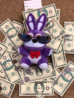 a purple stuffed animal with sunglasses on it's head and some money around it