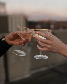 two people toasting with wine glasses on top of a roof in front of a cityscape