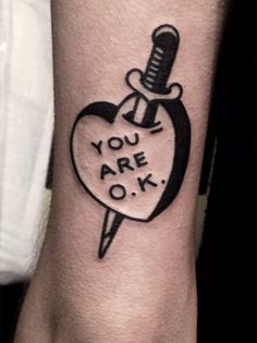 a black and white tattoo on the wrist that says you are ok with a knife sticking out of it