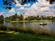 a boat is on the water in front of some trees and buildings with clouds above it