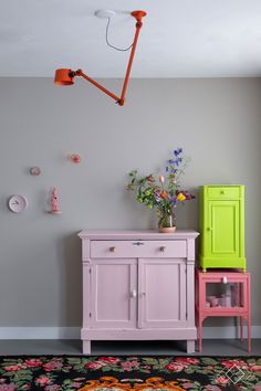 a pink and green sideboard next to a yellow cabinet in a room with grey walls