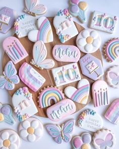 decorated cookies are arranged in the shape of rainbows, clouds, and butterflies on a wooden board