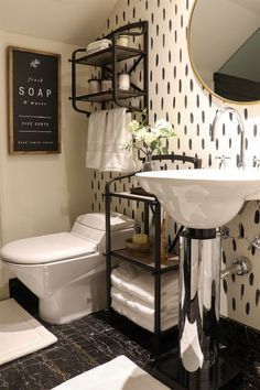 a white toilet sitting next to a sink in a bathroom under a mirror and a shelf with towels on it