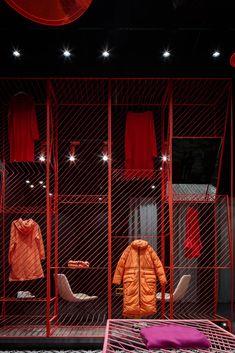 an orange jacket is on display in a red room with other clothing and accessories behind it