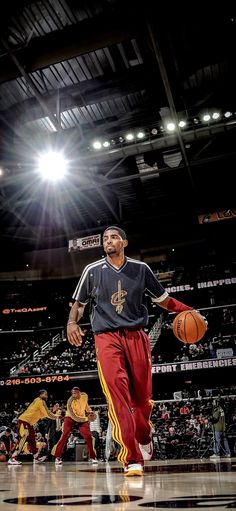 a man holding a basketball while standing on top of a basketball court with other people in the background