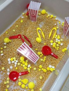 popcorn and other items in a bathtub filled with corn kernels, plastic spoons and red handled utensils