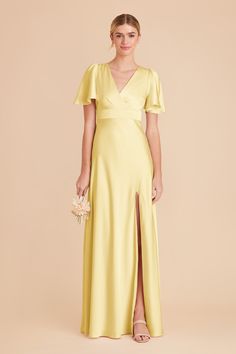 a woman wearing a yellow dress with a slit down the side and a flower in her hand