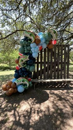 a bunch of balloons that are on top of a wooden bench in the grass next to a tree