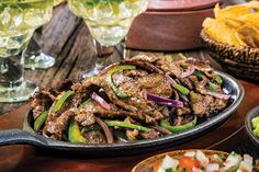 an assortment of mexican food on a wooden table with glasses and salsa in the background