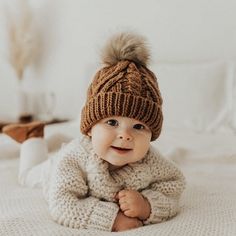 a baby wearing a knitted hat and sweater laying on a bed with white sheets