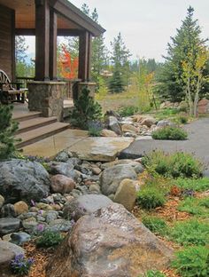 a house that has some rocks in the front yard and trees on the other side