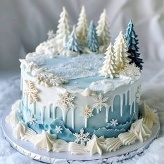 a blue and white frosted cake decorated with snowflakes, trees and icing