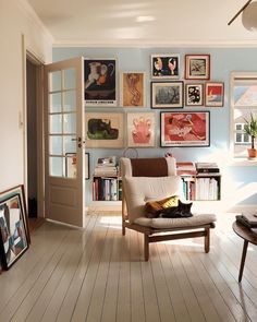 a living room with pictures on the wall and a cat sitting on a chair in front of it