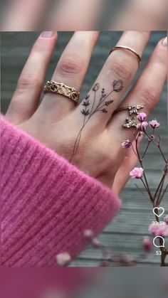 a woman's hand with tattoos on her fingers and flowers in the middle of it