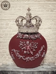 a large red vase with a crown on it's top sitting in front of a brick wall