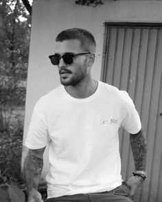 a man with tattoos and sunglasses sitting on a skateboard in front of a building