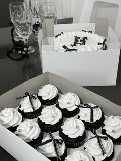 a box filled with lots of cupcakes covered in white frosting next to wine glasses