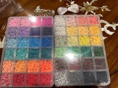 two plastic trays filled with different colored beads on top of a wooden table next to flowers