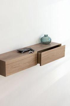 a wooden shelf with two drawers and a vase sitting on it's side, against a white wall