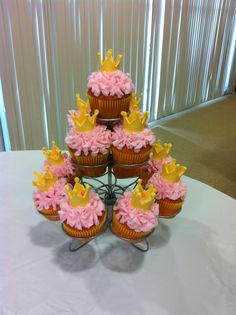 cupcakes with pink frosting and yellow crowns are arranged on a cake stand