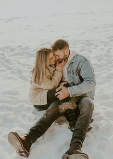 a man and woman sitting in the snow with their arms around each other as they kiss