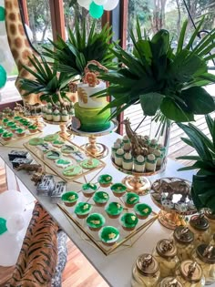 a table topped with cupcakes and cookies next to a potted palm tree