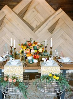 the table is set with yellow and orange flowers, candles, plates and napkins