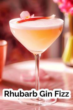 a close up of a drink in a glass on a table with flowers behind it and the words rhubarb gin fizz