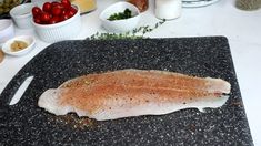 a raw fish sitting on top of a cutting board next to bowls of fruit and vegetables