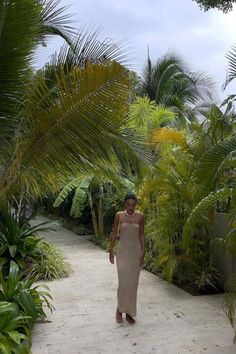 a woman in a dress walking down a path between palm trees and other tropical plants