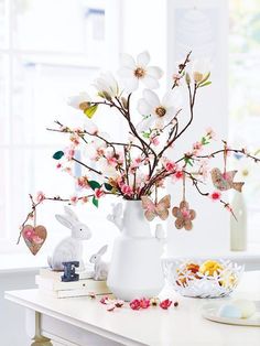 a white vase filled with flowers on top of a table next to a bowl of cookies