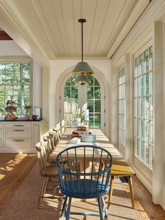 a long table with blue chairs in the middle of a room next to two windows