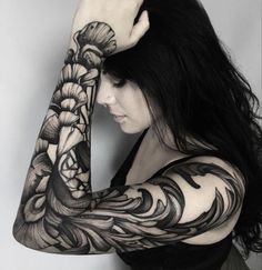 a woman with long black hair and tattoos on her arm, holding her hands behind her head