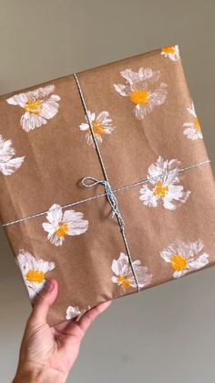 a person holding a wrapped present in brown paper with white and yellow flowers on it