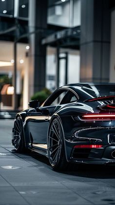 a black sports car parked in front of a building with its lights on at night