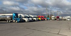 a row of semi trucks parked next to each other in a parking lot on a cloudy day