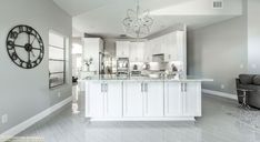 a large kitchen with white cabinets and marble counter tops, along with a gray couch