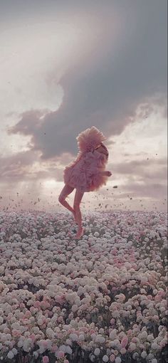 a woman in a pink dress is flying through the air over a field of flowers