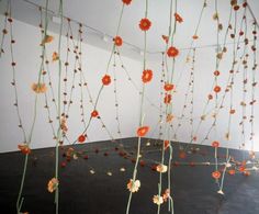 an arrangement of flowers in a room with white walls and black flooring, hanging from the ceiling