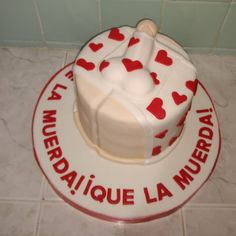 a white cake with red hearts on it sitting on top of a tile floor next to a tiled wall