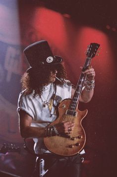 a man in a top hat playing an electric guitar on stage with red lights behind him