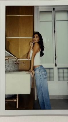 a woman standing in front of a sink talking on a cell phone and leaning against the wall