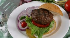 a hamburger with lettuce, tomato and onion on a plate next to tomatoes