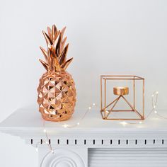 a gold pineapple candle holder sitting on top of a white mantle next to a small box