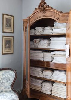 an old wooden bookcase filled with lots of papers next to a chair and pictures on the wall