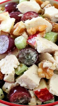 a close up of a bowl of food with grapes, chicken and nuts in it