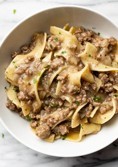 a white bowl filled with pasta covered in ground beef and sauce on top of a marble table