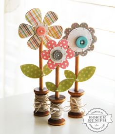 three wooden flowers with buttons on them sitting on a table next to twine spools