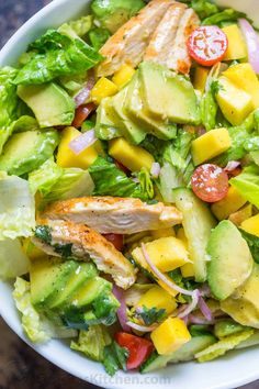 a salad with chicken, avocado, tomatoes and lettuce in a white bowl