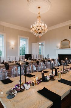 a long table with candles and flowers on it in front of a chandelier